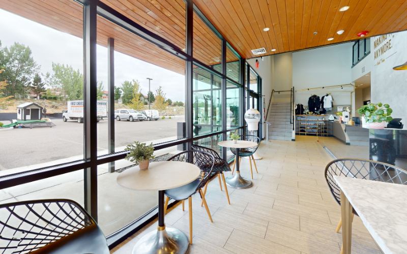 A bright and modern office lobby featuring large windows, round tables, black chairs, wood ceiling panels, and a reception desk in the background, creating a clean and inviting space.